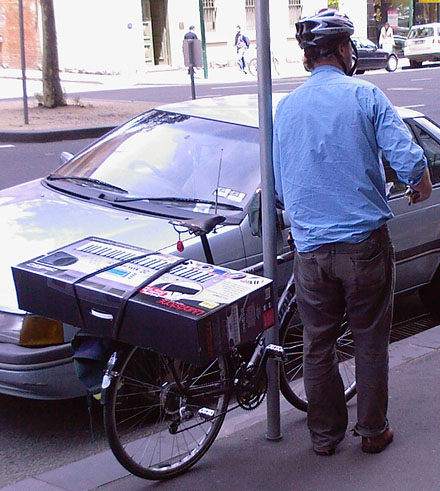 Man loads a large electronic keyboard onto the back of a bike.